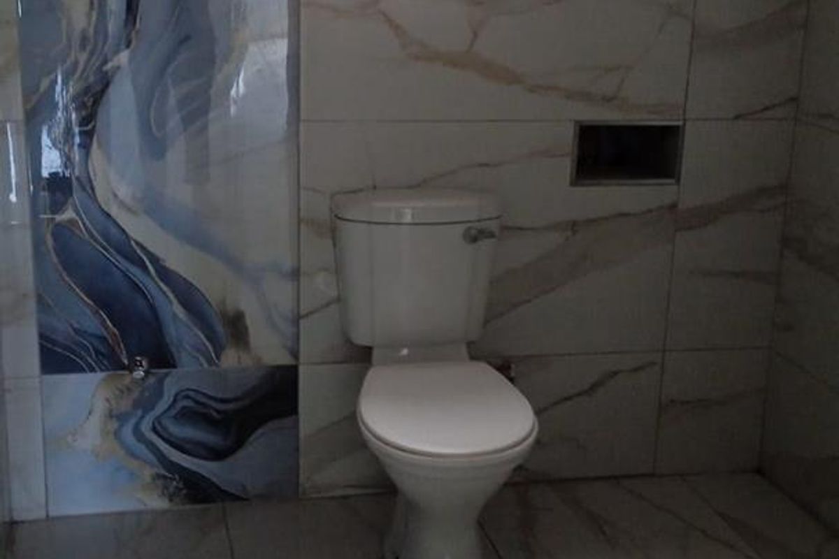 A modern bathroom featuring marble-effect wall and floor tiles, a white toilet, and a recessed wall niche.