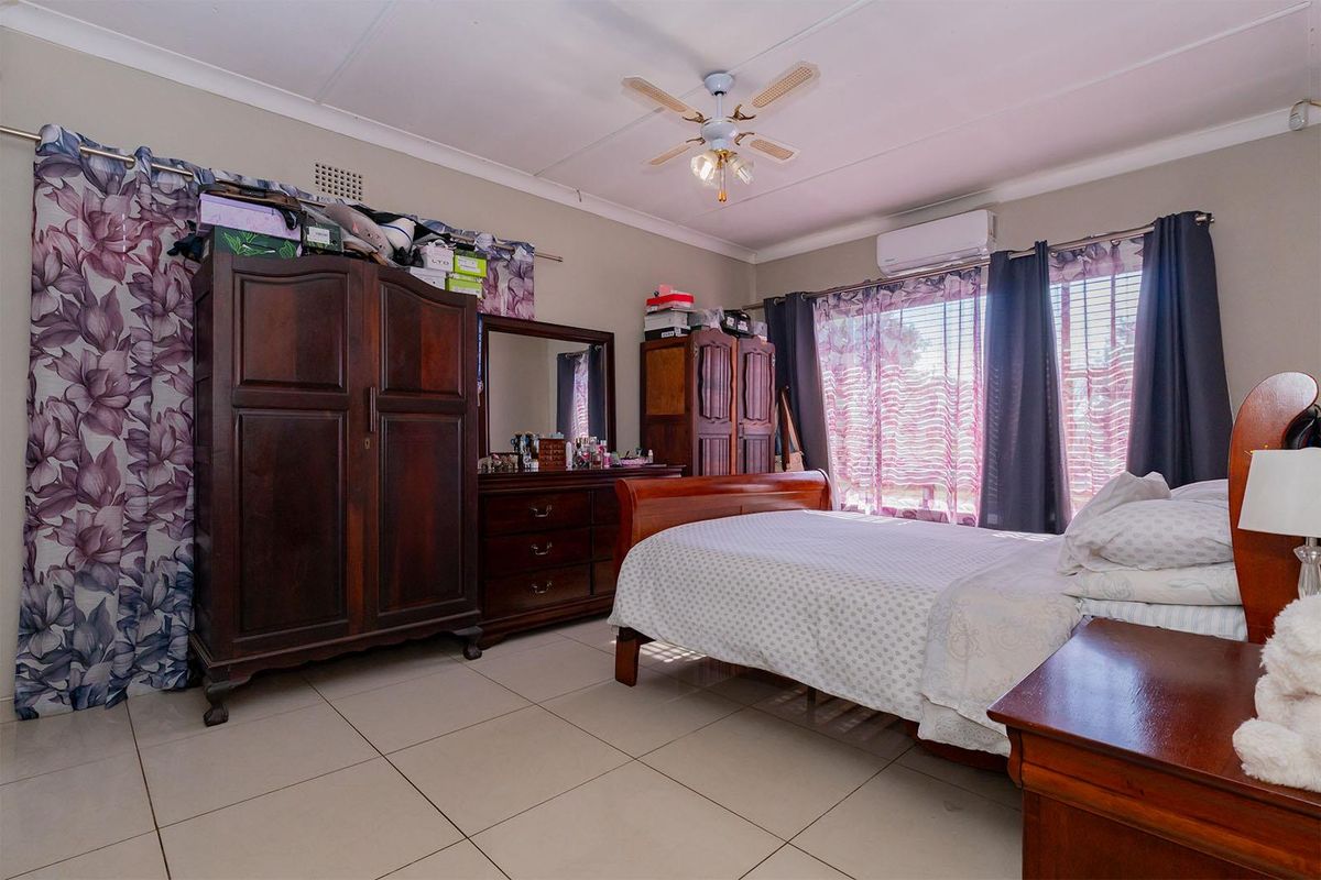 A spacious bedroom featuring tiled flooring, a ceiling fan, and a wall-mounted air conditioning unit.