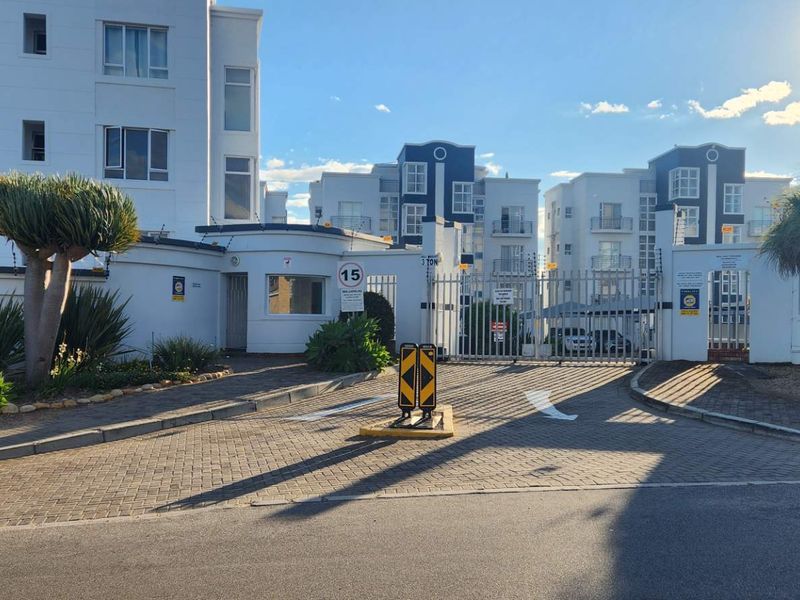The secure entrance to the apartment complex features a gated access point, guard house, and paved driveway with perimeter security fencing.