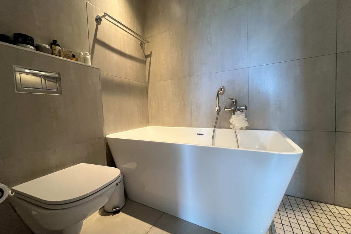 Modern bathroom featuring a sleek freestanding bathtub, wall-mounted toilet with concealed cistern, and large-format neutral wall tiles.