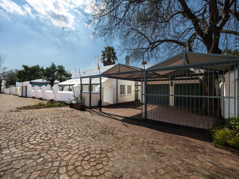 Front exterior view featuring a cobblestone driveway, secure carport, and perimeter wall with electric fencing.