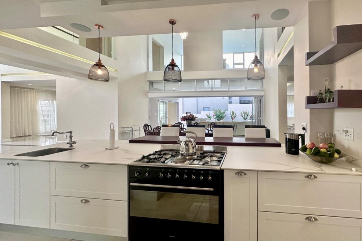 Modern open-plan kitchen featuring a large island with a gas hob, stone countertops, and elegant pendant lighting, overlooking a spacious living area.