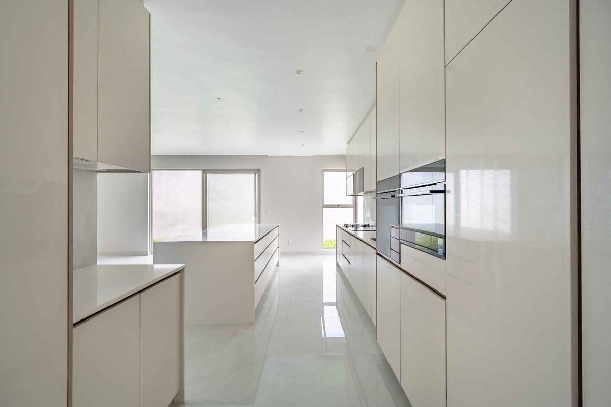 Modern, minimalist kitchen featuring high-gloss cabinetry, integrated appliances, a central island, and sleek tiled flooring in a bright, open-plan layout.