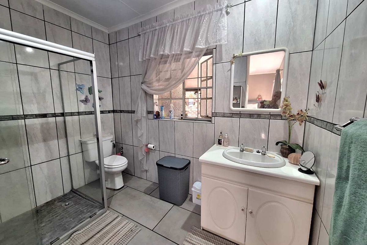 A functional bathroom featuring a glass-enclosed shower, a vanity with a basin, and full-height wall tiling.