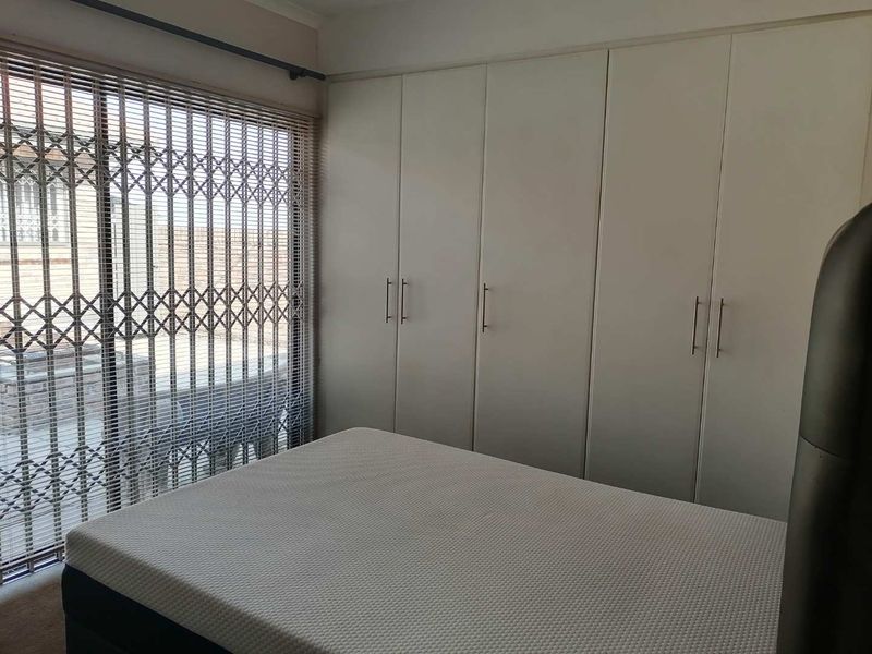 A bedroom featuring floor-to-ceiling built-in cupboards, a large window with venetian blinds, and a security gate for added protection.