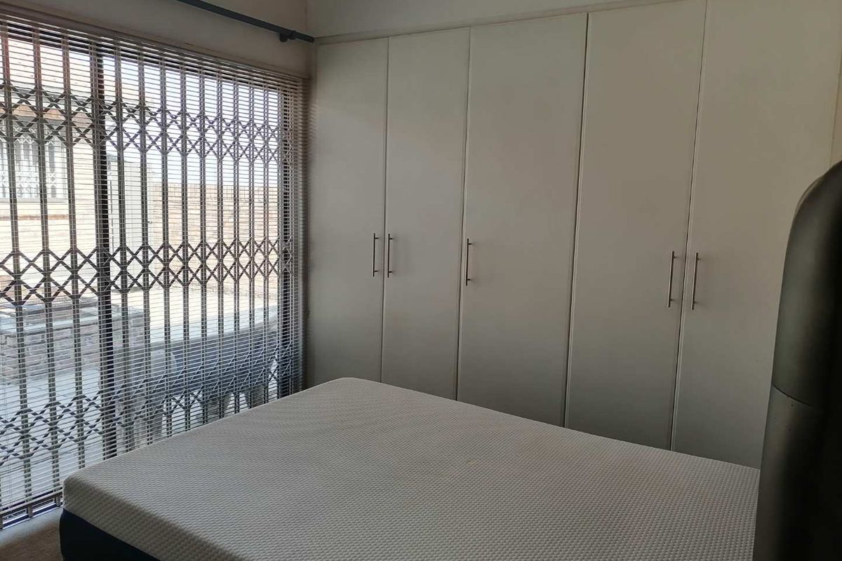A bedroom featuring floor-to-ceiling built-in cupboards, a large window with venetian blinds, and a security gate for added protection.