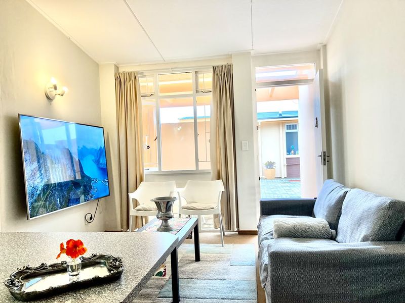 A bright living room featuring a wall-mounted television, large window, and direct access to an outdoor patio area.