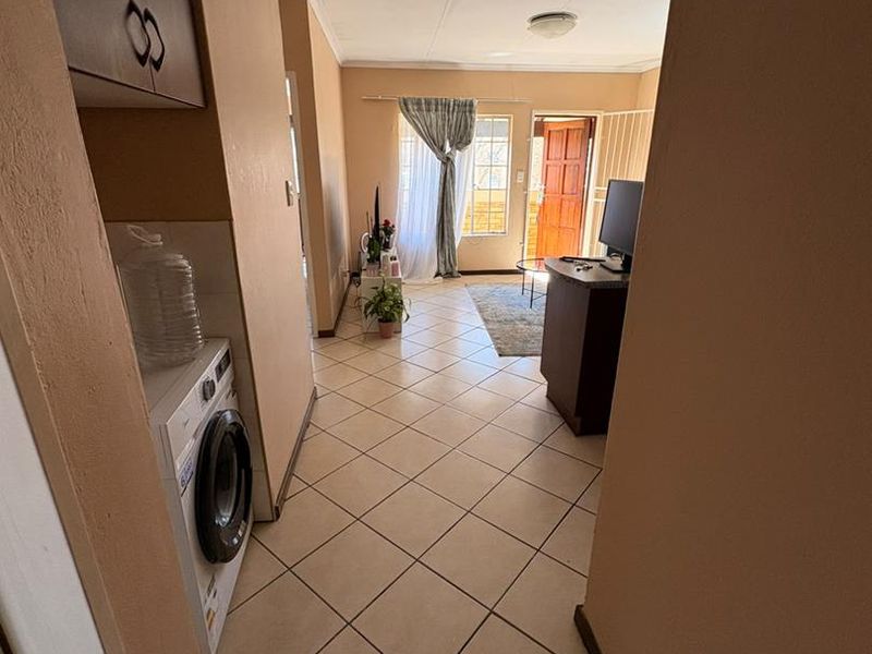 Open-plan living area featuring tiled flooring, built-in cabinetry, and a dedicated laundry space with plumbing connections, leading to an exterior entrance.