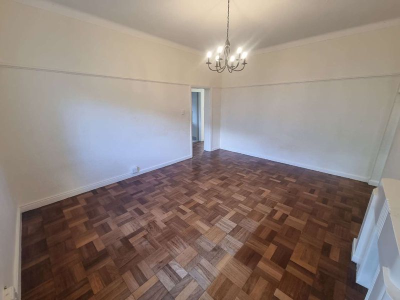An empty living room featuring classic parquet flooring, coved ceilings, and a decorative chandelier, offering a blank canvas for interior design.