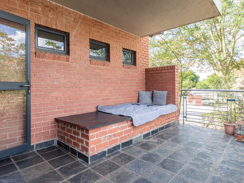 A covered balcony featuring a built-in brick bench, slate tile flooring, and an exposed brick wall with aluminium framed windows.