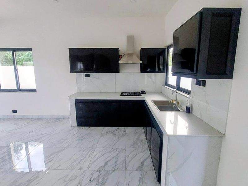 Modern open-plan kitchen featuring sleek black cabinetry, white marble-look countertops, integrated gas hob, extractor fan, and matching marble-effect floor tiles.