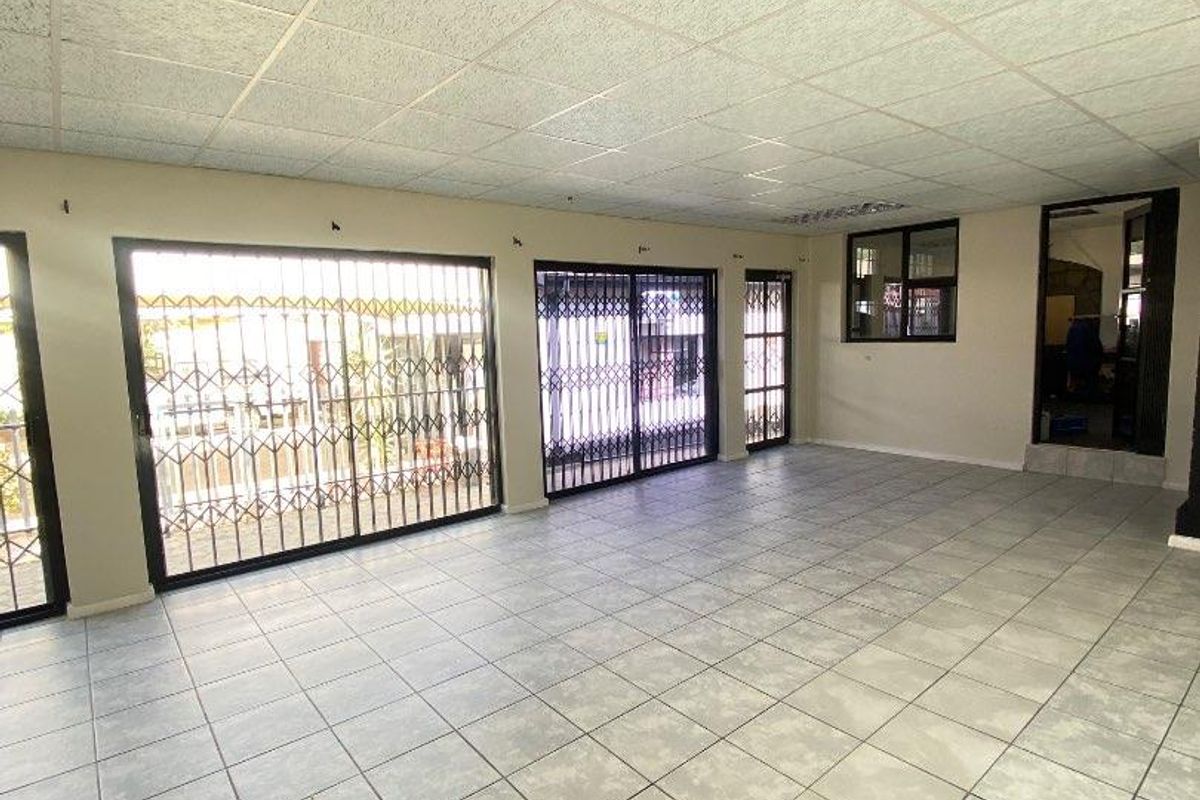 Spacious, empty living area featuring tiled flooring, a drop ceiling, and multiple sliding doors with security gates leading to the exterior.