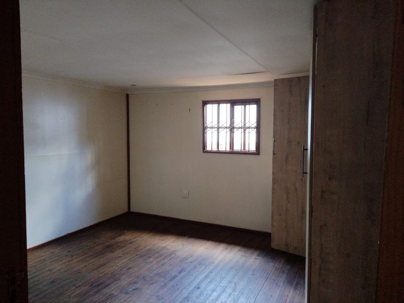 An empty bedroom featuring timber flooring, a built-in wardrobe, and a window fitted with security bars.