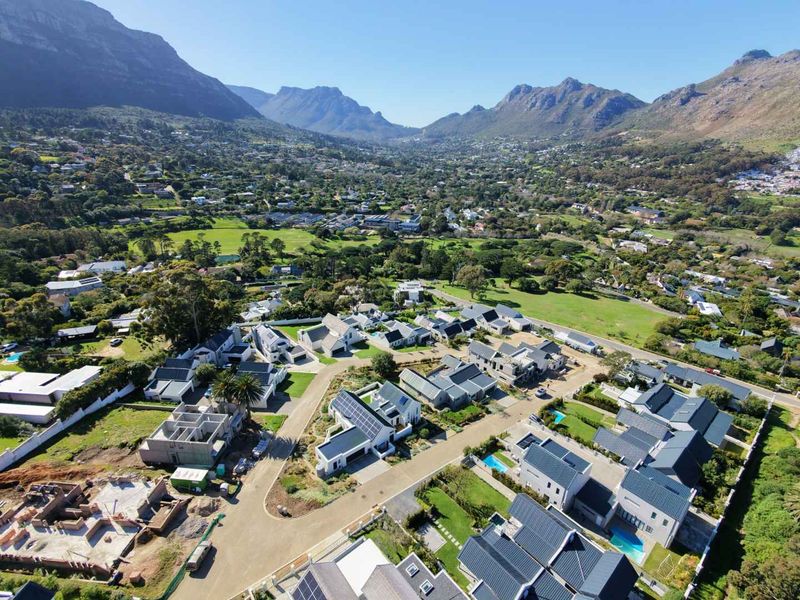 Aerial view of a modern residential estate featuring multiple homes with solar panels, swimming pools, and landscaped gardens set against a mountain backdrop.