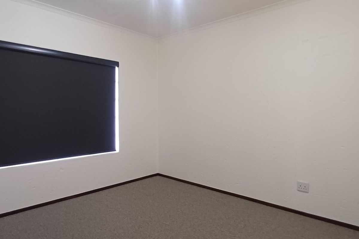 A clean, empty bedroom featuring neutral carpet flooring, white walls, and a dark roller blind, providing a blank canvas for personalization.