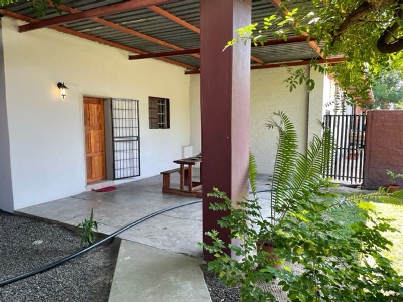 A covered outdoor patio area featuring concrete flooring, a corrugated metal roof, and a secure entrance with a wooden door and security gate.