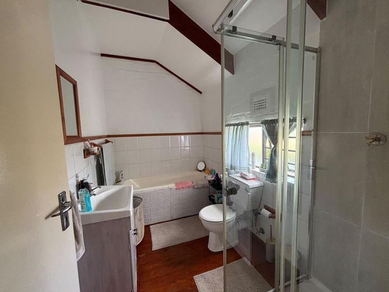 A functional bathroom featuring a bathtub, separate shower enclosure, toilet, and vanity basin, characterized by exposed timber beams and a sloped ceiling.
