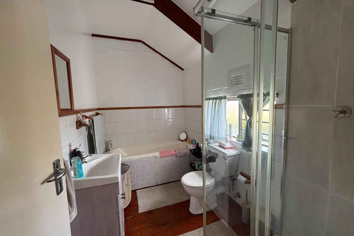 A functional bathroom featuring a bathtub, separate shower enclosure, toilet, and vanity basin, characterized by exposed timber beams and a sloped ceiling.