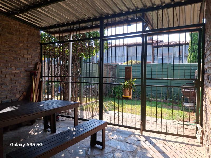 A covered patio area featuring stone paving, exposed brickwork, and a secure steel gate leading to a small private garden.