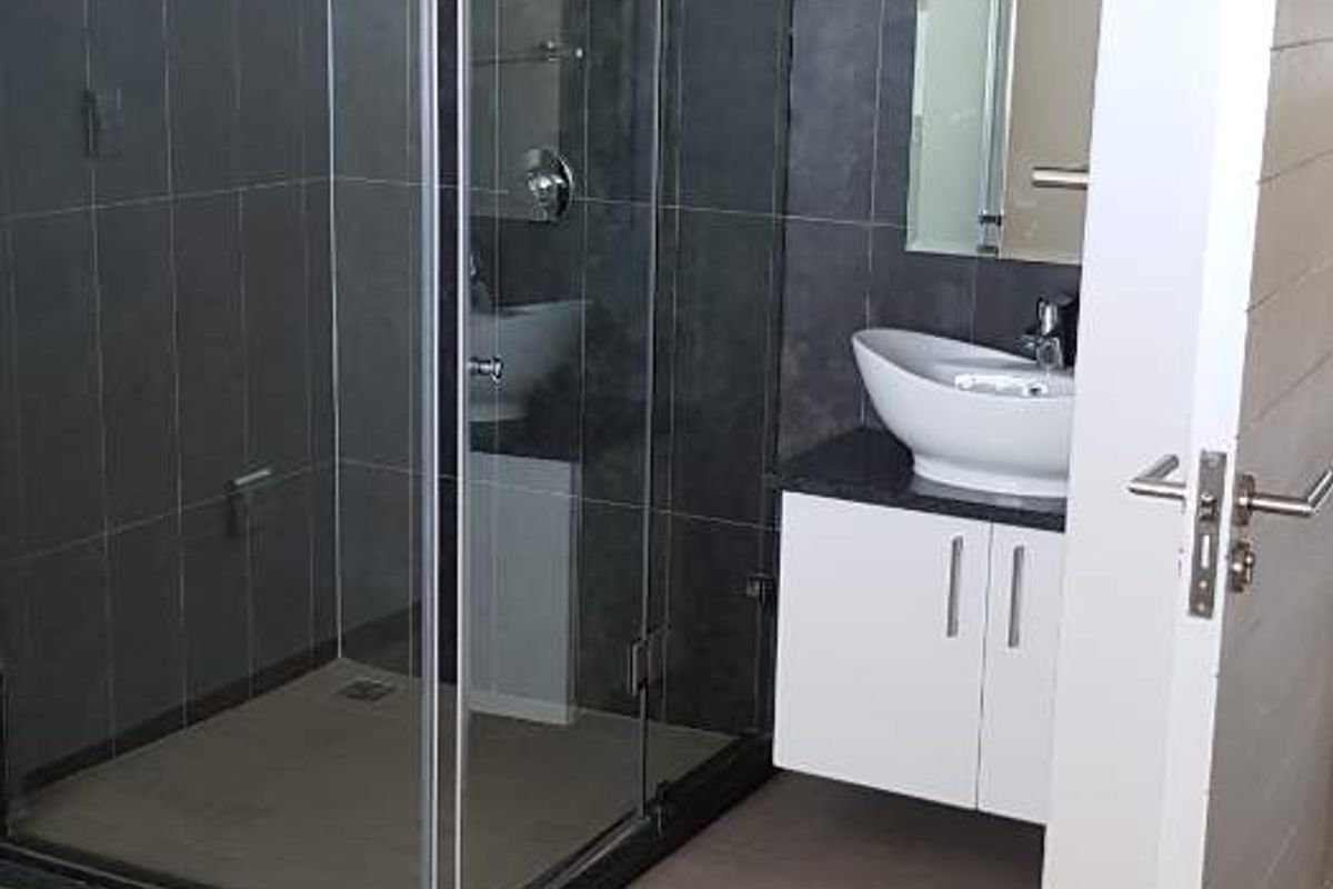 Modern bathroom featuring a glass shower enclosure, wall-mounted vanity with a vessel sink, and dark tiled wall finishes.