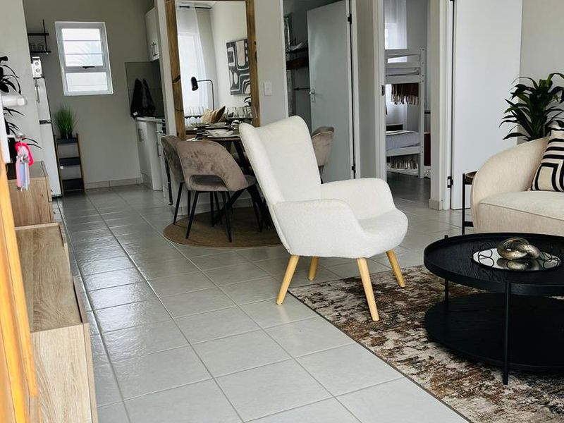 An open-plan living and dining area featuring light-colored tiled flooring, a high tongue and groove ceiling, and direct access to adjacent rooms.