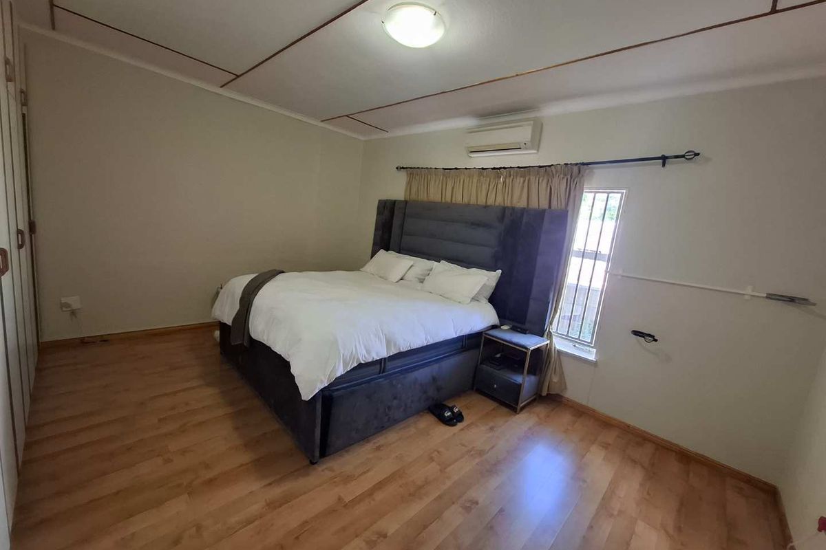 A functional bedroom featuring laminate flooring, built-in cupboards, and a wall-mounted air conditioning unit.