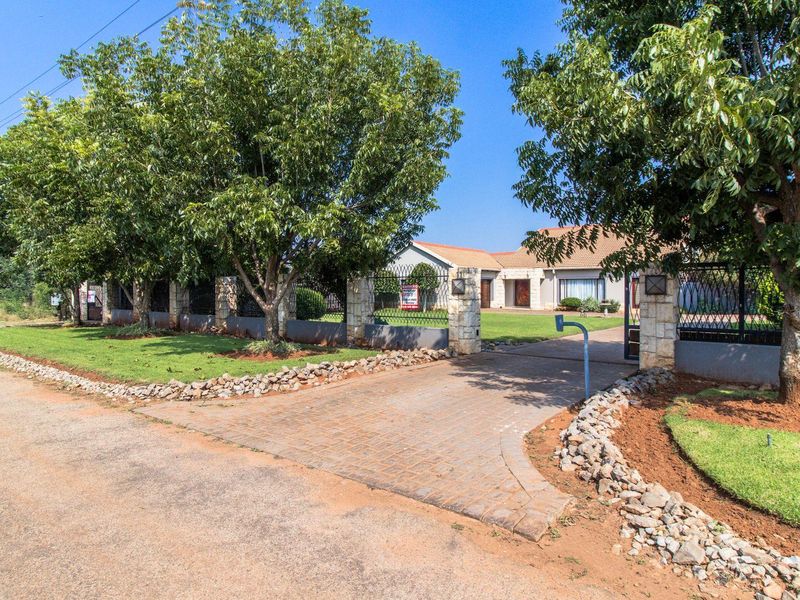 Front view of the property featuring a paved driveway, stone-clad boundary wall, wrought iron fencing, and a well-maintained garden.