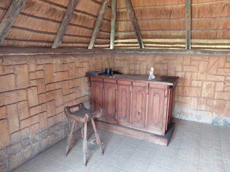 A rustic bar area featuring a thatched roof, exposed timber rafters, and a built-in wooden bar counter with tiled flooring.