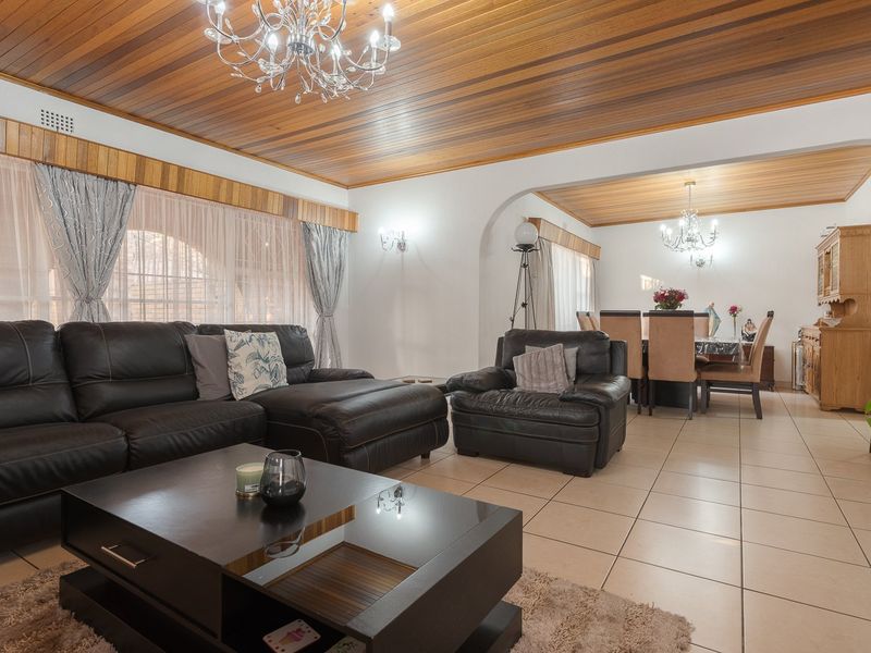 Spacious open-plan living and dining area featuring warm timber ceilings, ceramic floor tiles, and elegant crystal chandeliers, creating a comfortable and inviting atmosphere.