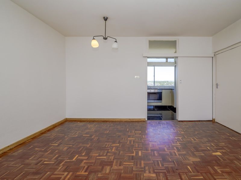 An empty living room featuring classic parquet flooring, a sliding door leading to the kitchen, and a simple ceiling light fixture.