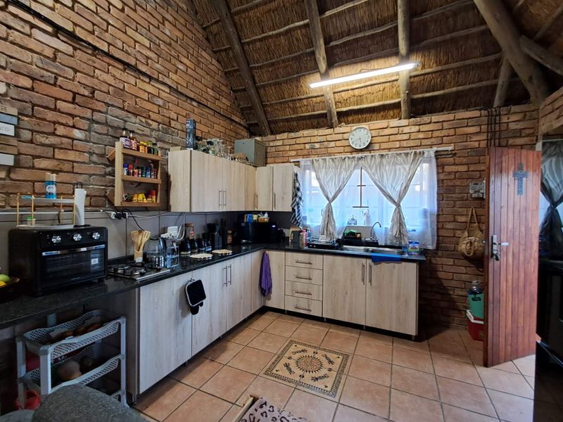 Rustic kitchen featuring exposed brick walls, a high thatched ceiling with timber rafters, laminate cabinetry, granite countertops, and tiled flooring.