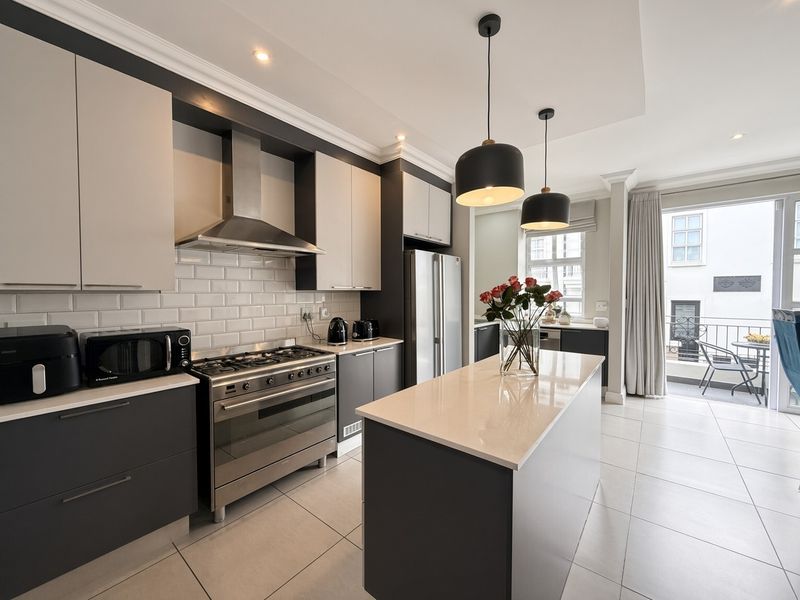 Modern kitchen featuring a central island, gas stove with extractor, subway tile backsplash, and sleek cabinetry, flowing seamlessly to an outdoor balcony area.