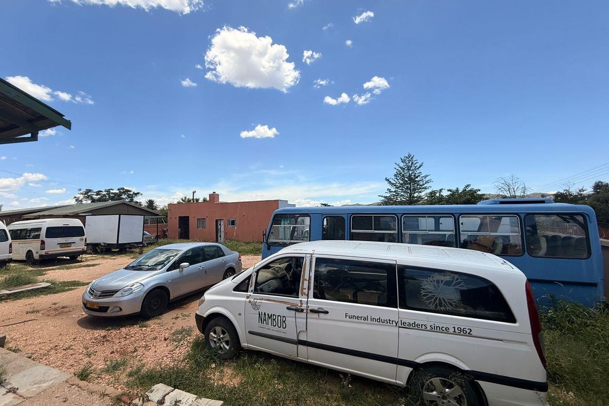 Exterior view of a property yard featuring multiple parked vehicles and a single-story building structure.