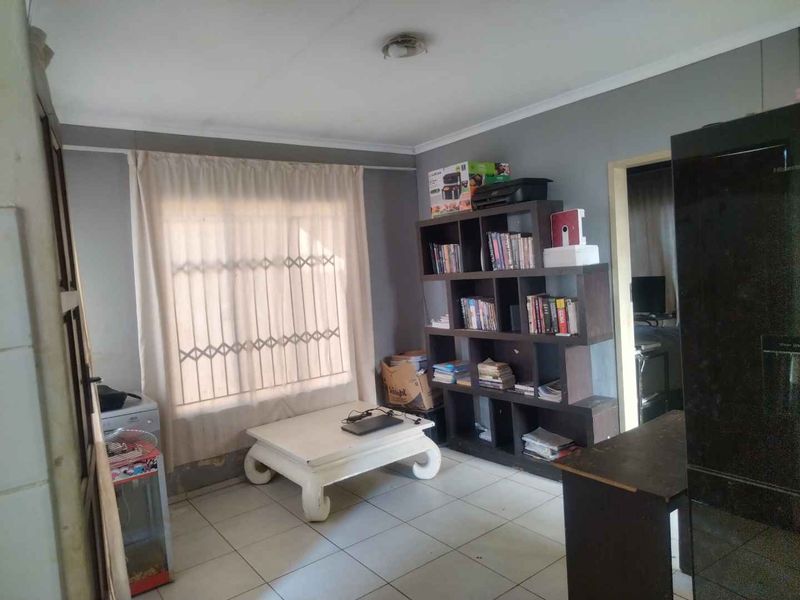 A living area featuring tiled flooring and a window with security bars, requiring minor cosmetic updates to the walls and lighting.