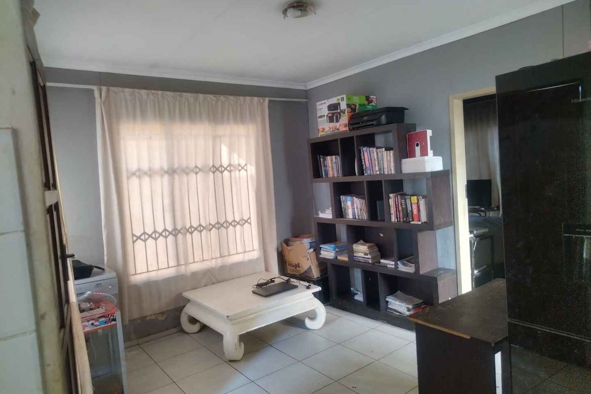 A living area featuring tiled flooring and a window with security bars, requiring minor cosmetic updates to the walls and lighting.
