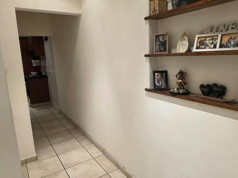 A functional hallway featuring built-in wooden wall shelving and neutral ceramic floor tiles, providing a clean transition between living spaces.
