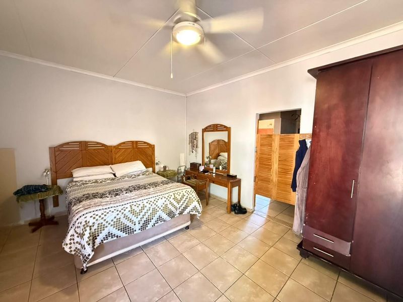 A spacious bedroom featuring tiled flooring, a ceiling fan, and direct access to an adjoining room through a wooden door.