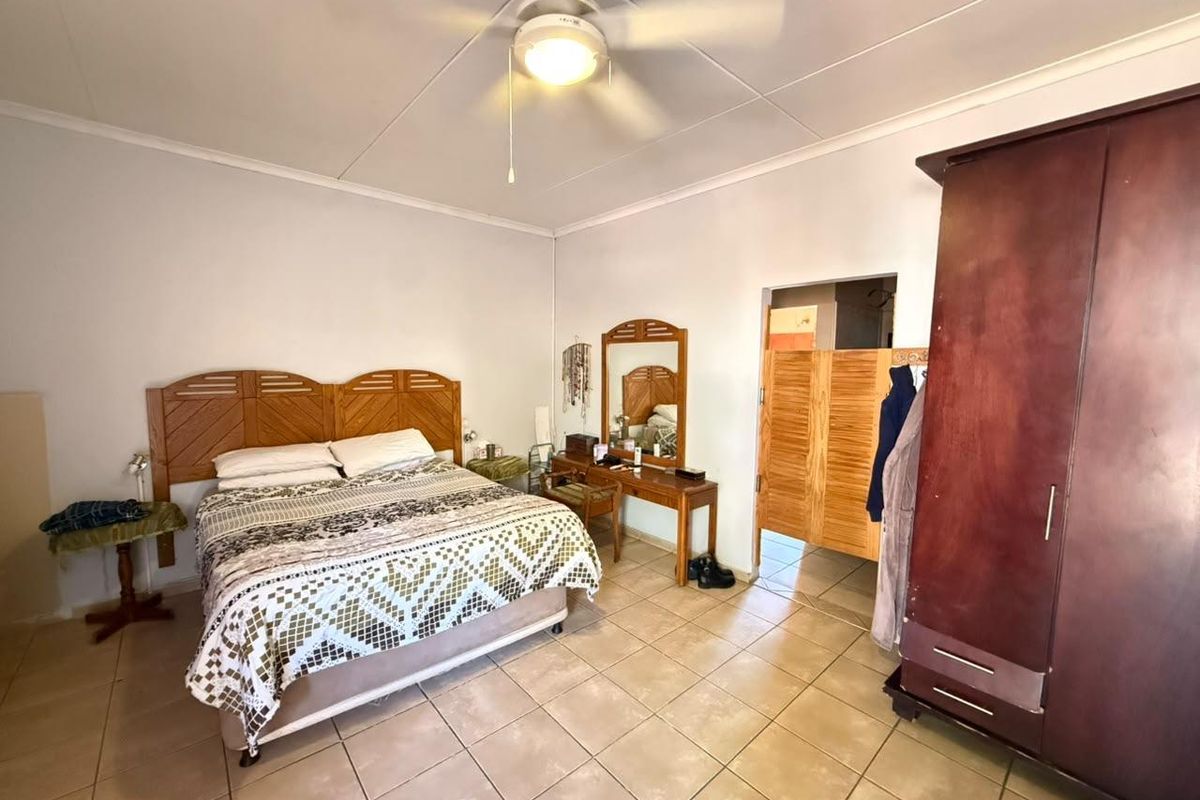 A spacious bedroom featuring tiled flooring, a ceiling fan, and direct access to an adjoining room through a wooden door.