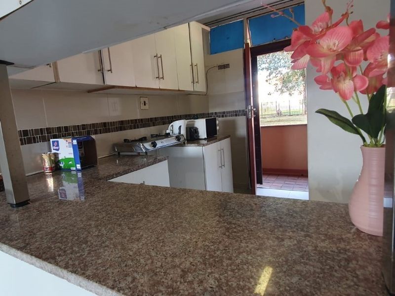A functional kitchen featuring granite countertops, built-in cabinetry, and a tiled backsplash, with direct access to an outdoor balcony area.