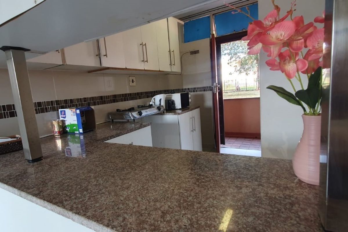 A functional kitchen featuring granite countertops, built-in cabinetry, and a tiled backsplash, with direct access to an outdoor balcony area.