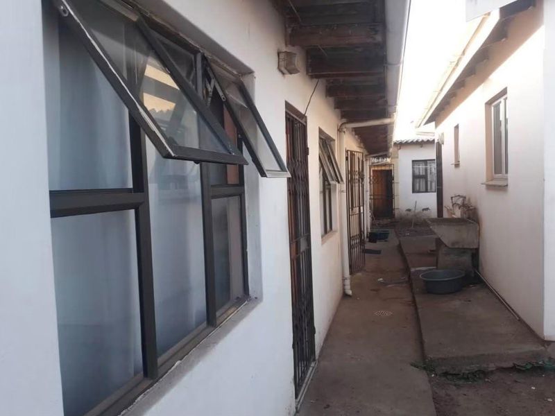 A narrow exterior side passage featuring concrete flooring, security gates, aluminium windows, and an external utility wash basin.