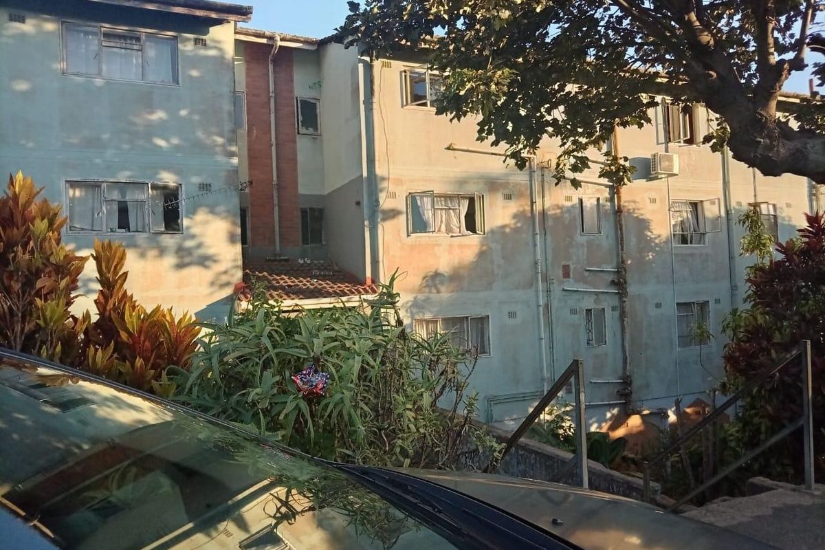 Exterior view of a multi-story apartment building showing weathered facade, casement windows, and external plumbing infrastructure.