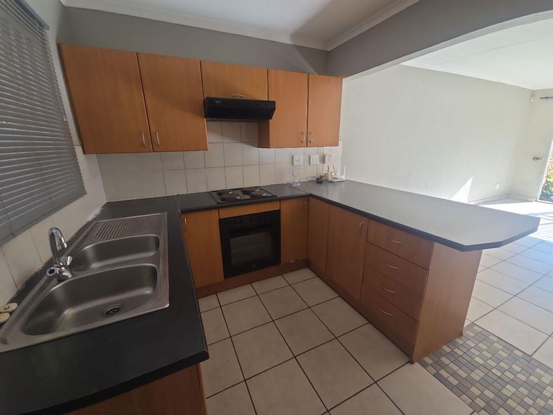 A functional kitchen featuring laminate cabinetry, built-in oven, electric hob, and a double bowl stainless steel sink with tiled flooring.