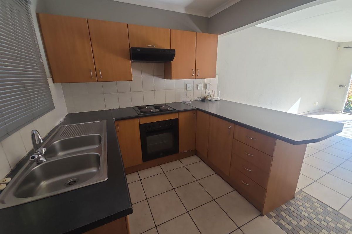 A functional kitchen featuring laminate cabinetry, built-in oven, electric hob, and a double bowl stainless steel sink with tiled flooring.