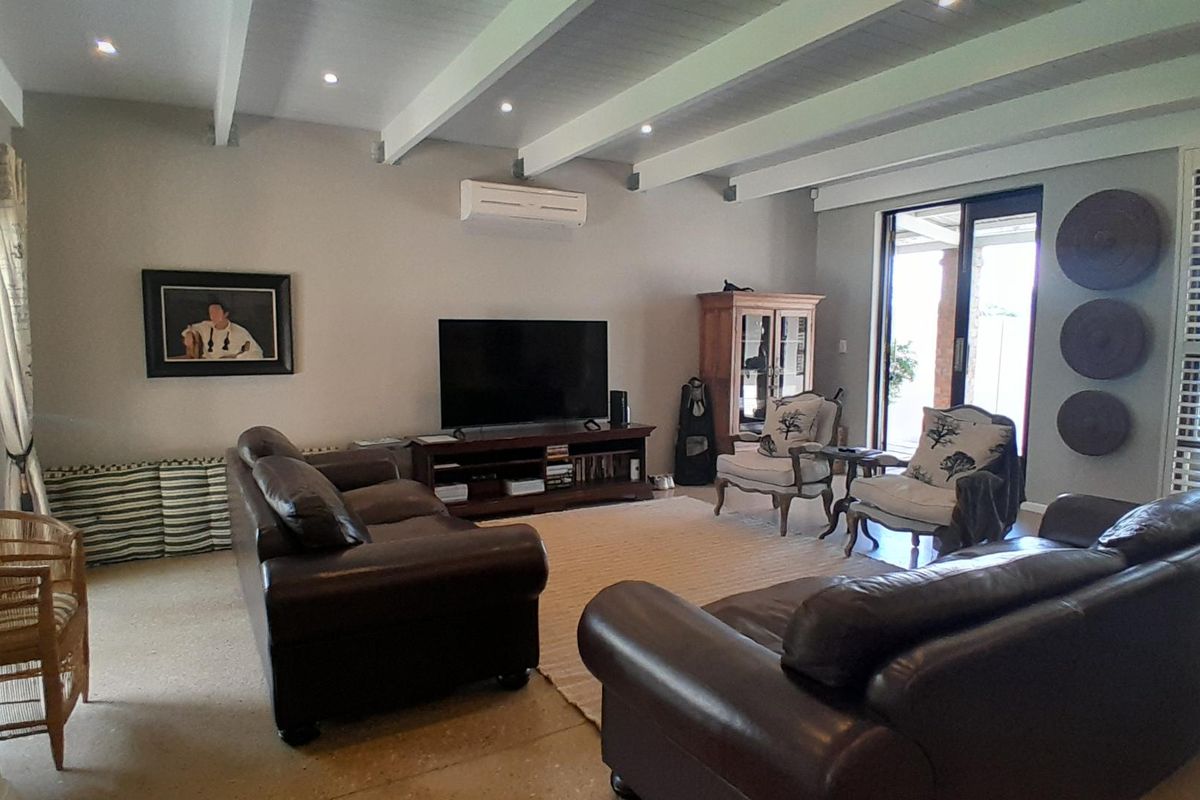 Spacious living room featuring exposed ceiling beams, recessed lighting, a split-system air conditioner, and large sliding glass doors leading to the outdoor area.