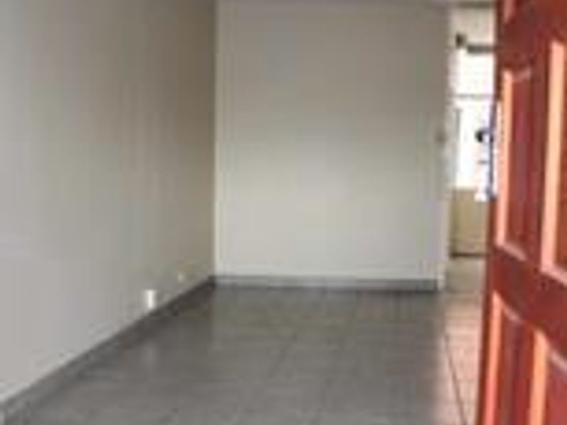 An empty, neutrally painted living area featuring tiled flooring and a wooden entrance door, offering a blank canvas for personalization.