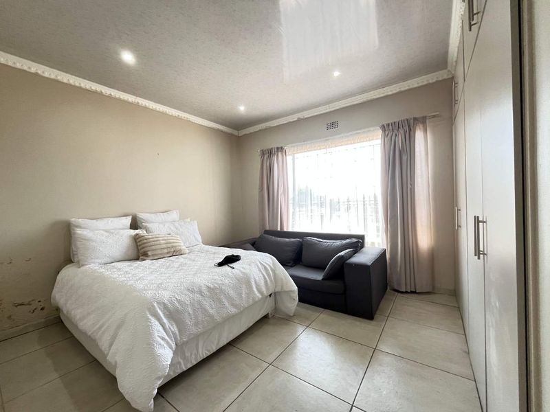 A bedroom featuring tiled flooring, built-in cupboards, and recessed lighting. Note visible wall staining requiring attention.
