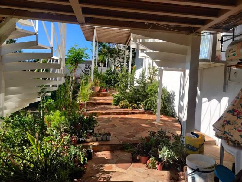 A covered outdoor patio area featuring stone paving, a white spiral staircase, and structural support columns, providing a functional transition space to the garden.