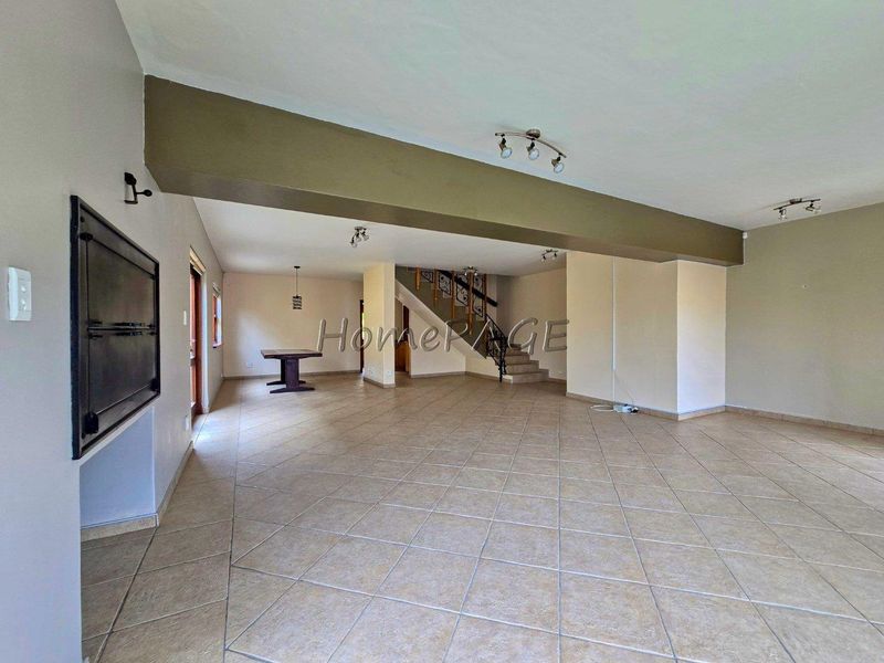 Spacious open-plan living area featuring tiled flooring, a built-in fireplace, and a central staircase with a wooden balustrade.