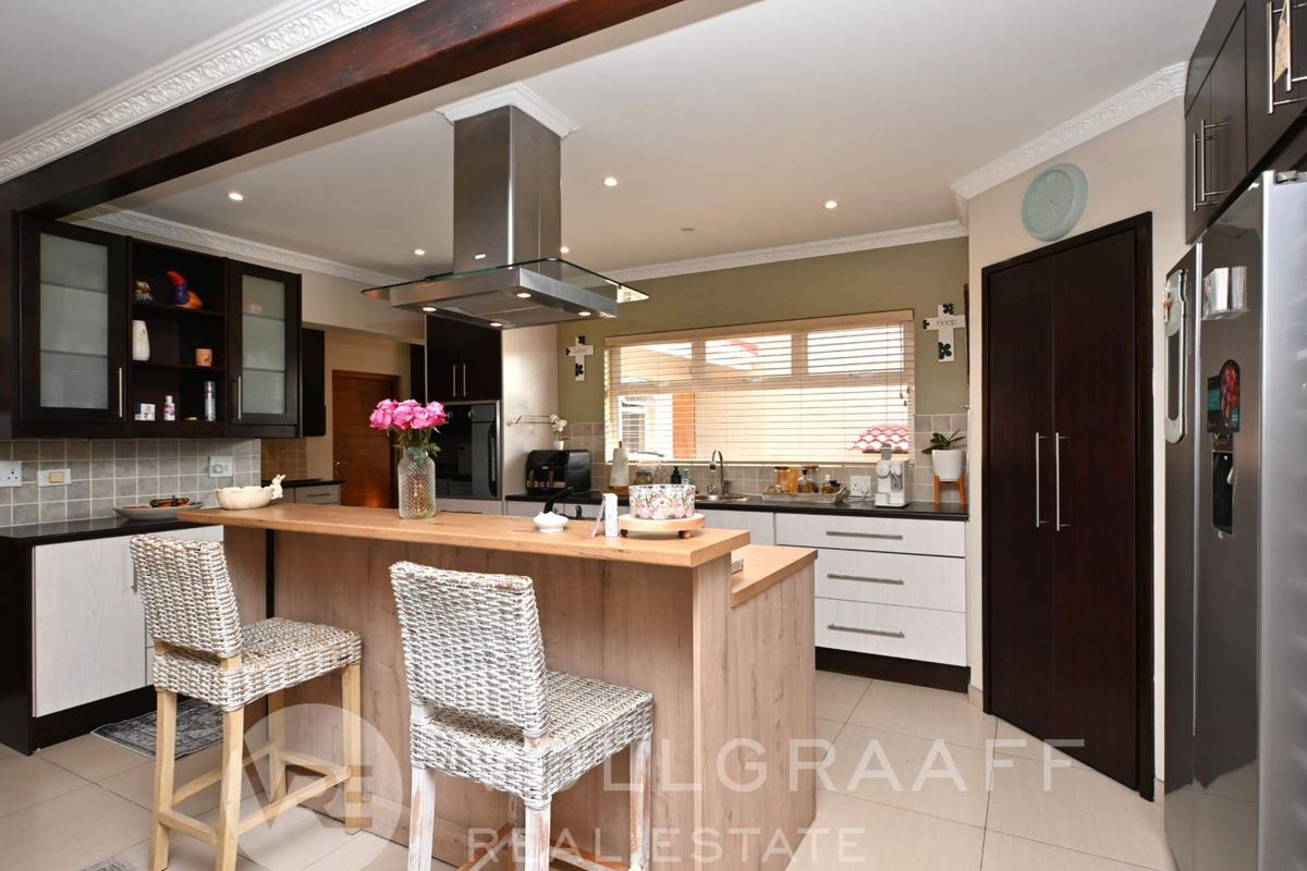 Modern kitchen featuring a breakfast bar, stainless steel extractor fan, tiled flooring, and dark wood cabinetry with integrated storage solutions.